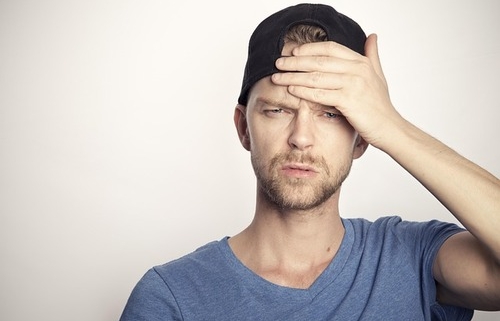 a man wearing a baseball cap holds his hand to his forehead